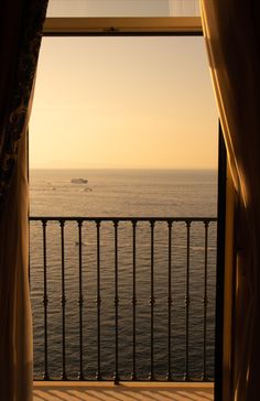 an open window overlooking the ocean and a boat in the distance with curtains on either side