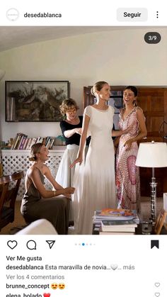 two women in dresses talking to each other while another woman sits on the couch behind them