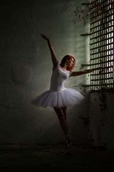 a young ballerina is posing in the dark with her arms stretched out and one leg up