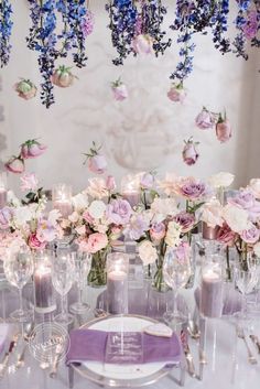 the table is set with purple and white flowers in vases, silverware, and candles