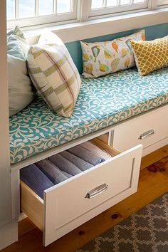 a window seat with drawers underneath it and pillows on the bench in front of it