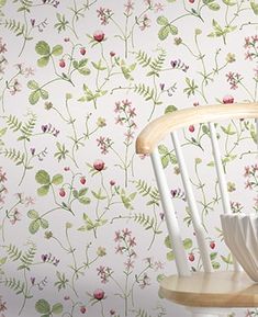 a white chair sitting in front of a wallpapered with pink and green flowers