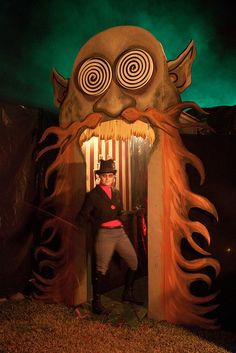 a man standing in front of a fake monster with his hands on his hips while wearing a hat