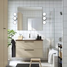 a bathroom with white tiled walls and flooring is shown in this image, there are three round lights on the mirror above the sink