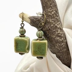 Handmade rustic ceramic beaded earrings. Olive green in color. Smaller in size at 1.5 inches long by .50 inches wide. The square bead is glazed ceramic with a complimenting Czech glass bead at the top. Paired with bronze wires, hooks, and accent beads, these make a perfect casual, rustic style. They would be great for fall. Give them as an affordable gift, or keep them for yourself.  LENGTH: 1.5 inches long WIDTH: .50 wide All of my earrings come with a soft, flexible rubber back that will help Cute Affordable Beaded Earrings For Gifts, Affordable Rustic Jewelry For Gifts, Cheap Artisan Green Earrings, Affordable Handmade Glass Beaded Earrings, Affordable Artisan Green Earrings, Affordable Earrings With Dangling Beads, Affordable Beaded Czech Glass Earrings, Earthy Green Earrings, Affordable Handmade Dangle Beads