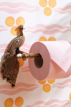 a pink toilet paper holder with a gold peacock on it and a pink roll of toilet paper