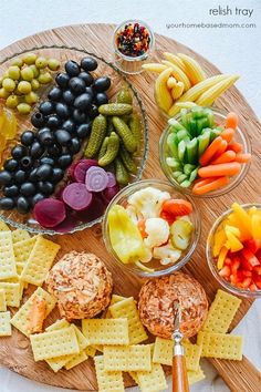 a platter with crackers, olives, carrots, grapes and celery