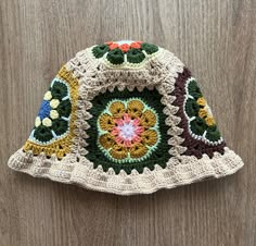 a crocheted hat with flowers and leaves on it sitting on a wooden surface