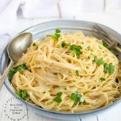 a plate of pasta with parsley on top and a fork in the bowl next to it