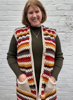 a woman standing in front of a brick wall wearing a multicolored crocheted vest