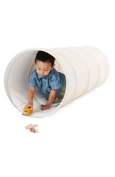 a little boy playing in a white tunnel with wooden pieces on the floor and one toy car coming out