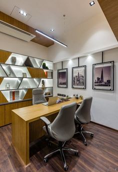 an office with two desks and chairs in front of the wall mounted bookshelves