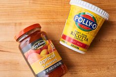 two jars of pickled fruit sitting on top of a wooden table next to each other