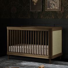 an empty crib in a dark room with floral wallpaper and framed pictures on the wall