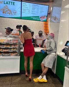 a woman in a red dress is ordering food at a donut shop with other people