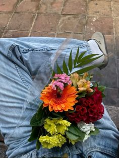 a man sitting on the ground with flowers in his lap and jeans rolled over him