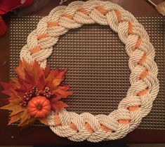 a white rope wreath with orange and red leaves on it sitting on top of a table