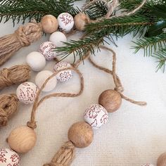 some ornaments are hanging from a tree branch on a white tablecloth with pine needles