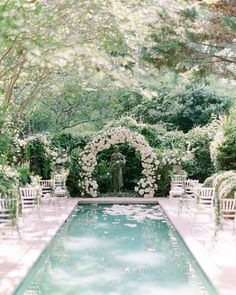 an outdoor wedding setup with white chairs and flowers on the side of the swimming pool