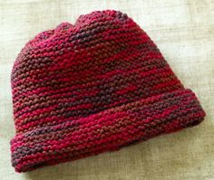 a knitted hat sitting on top of a white cloth covered in red and brown yarn