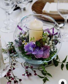 there is a glass bowl with flowers and a candle in it on top of the table