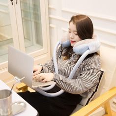 a woman sitting in a chair with a laptop on her lap and wearing a neck pillow