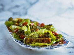 a plate filled with lettuce and tomatoes on top of a marble countertop