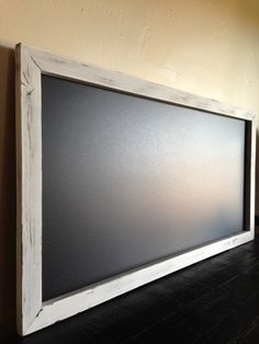 a white framed chalk board on a wooden floor in front of a wall with a black background