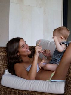 a woman sitting on top of a couch with a baby in her lap and pointing to the side