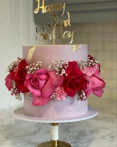 a pink and gold birthday cake with flowers on top