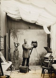 an old black and white photo of a man holding a camera in front of a painting