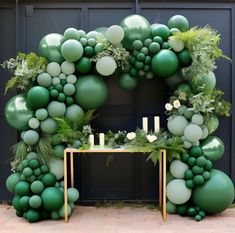 an arch made out of balloons and greenery with candles on the table in front of it