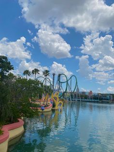 an amusement park with water and roller coasters in the background under a cloudy blue sky