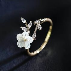 a gold ring with a flower and leaves on the front, sitting on a black surface