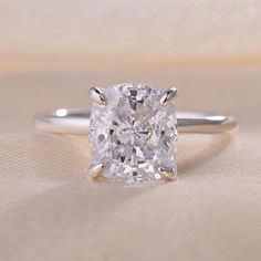 a cushion cut diamond sits on top of a white surface with a gold band around it