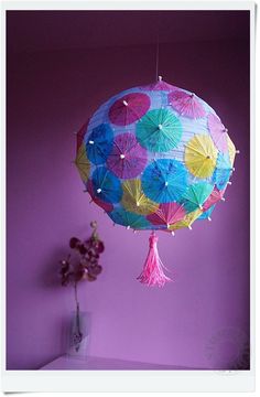 a colorful umbrella hanging from the ceiling next to a vase with purple flowers in it