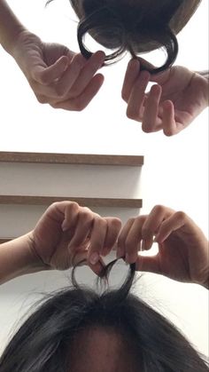 two hands holding scissors over the top of a woman's hair