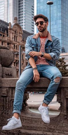 a man sitting on top of a stone bench next to tall buildings in the city