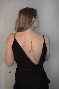 a woman in a black dress with a tattoo on her back and flowers behind her