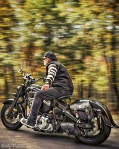 a man riding on the back of a motorcycle down a road in front of trees