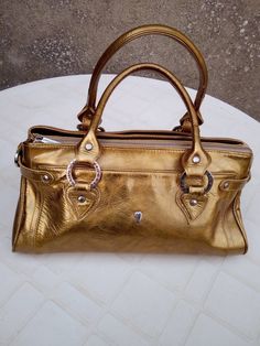 Superbe sac à main en cuir de la marque Lancaster , Largeur 35 cm , hauteur 16cm , profondeur 17 cm , 4 poches intérieures dont 1 zippée , 2 poches extérieures . À noter quelques auréoles d'origine en bas du sac  ( voir dernière photo ) mais très peu visible quand le sac est porté . Très bon état général , peu utilisé .Fabriqué en France .  Envoi Colissimo . Pas de retour ni échange . Gold Tote Bag With Palladium Hardware, Gold Leather Shoulder Bag With Metal Hardware, Luxury Metallic Bags With Zipper Closure, Gold Leather Bags With Metal Hardware, Gold Tote Satchel With Zipper Closure, Gold Shoulder Bag With Palladium Hardware, Gold Leather Satchel With Handles, Metallic Leather Bags With Gold-tone Hardware, Gold Leather Bags With Handles