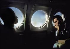 a man sitting in an airplane looking out the window at another person standing next to him