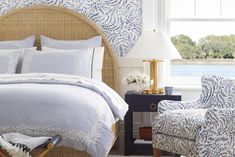 a bedroom with blue and white bedding in front of a window next to a chair