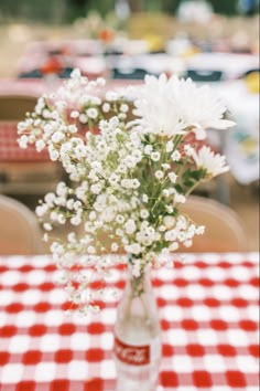 a vase filled with white flowers sitting on top of a red and white checkered table cloth