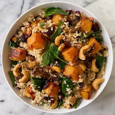 a white bowl filled with rice, nuts and spinach on top of a marble table