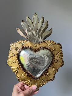 a heart shaped brooch is held up in front of a gray background with gold accents