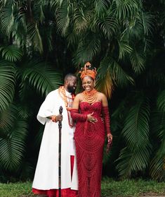 a man and woman standing next to each other in front of palm trees wearing red dresses