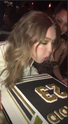 a woman holding up a cake with gold letters on it