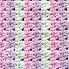 the crocheted blanket is pink, white and purple with stripes on it's sides