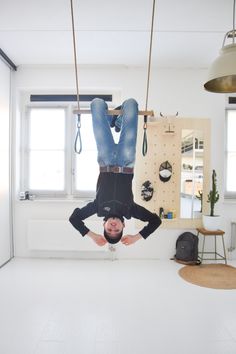 a man hanging upside down on a rope in a room with white walls and flooring